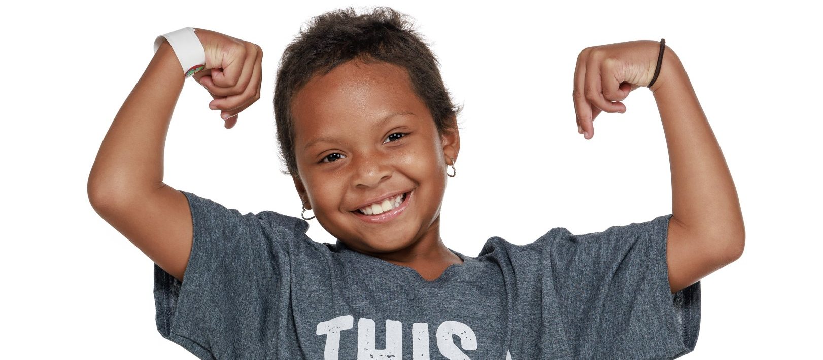 St. Jude patient Kinsley flexes her arms and smiles while wearing a This Shirt Saves Live T-shirt.