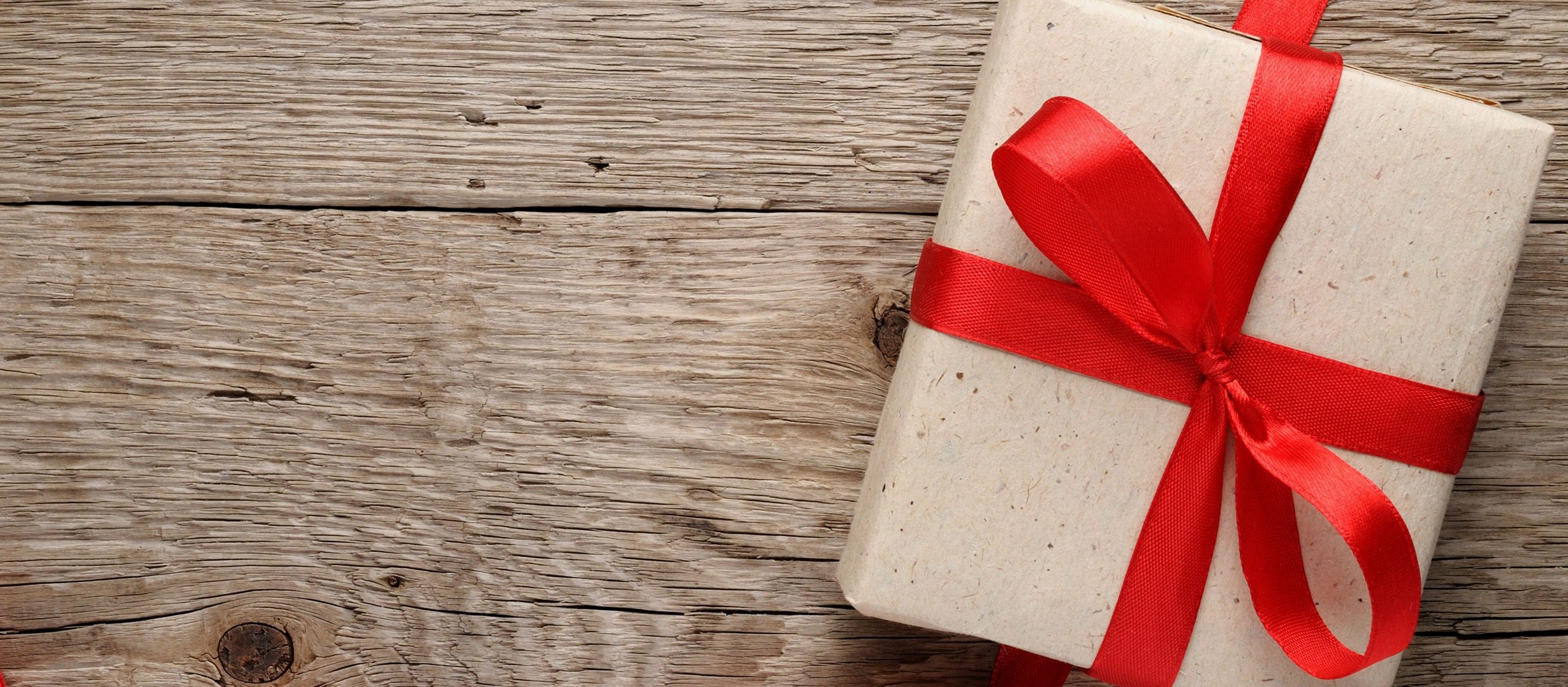 A wrapped package with a large red bow sits on a rustic wooden table