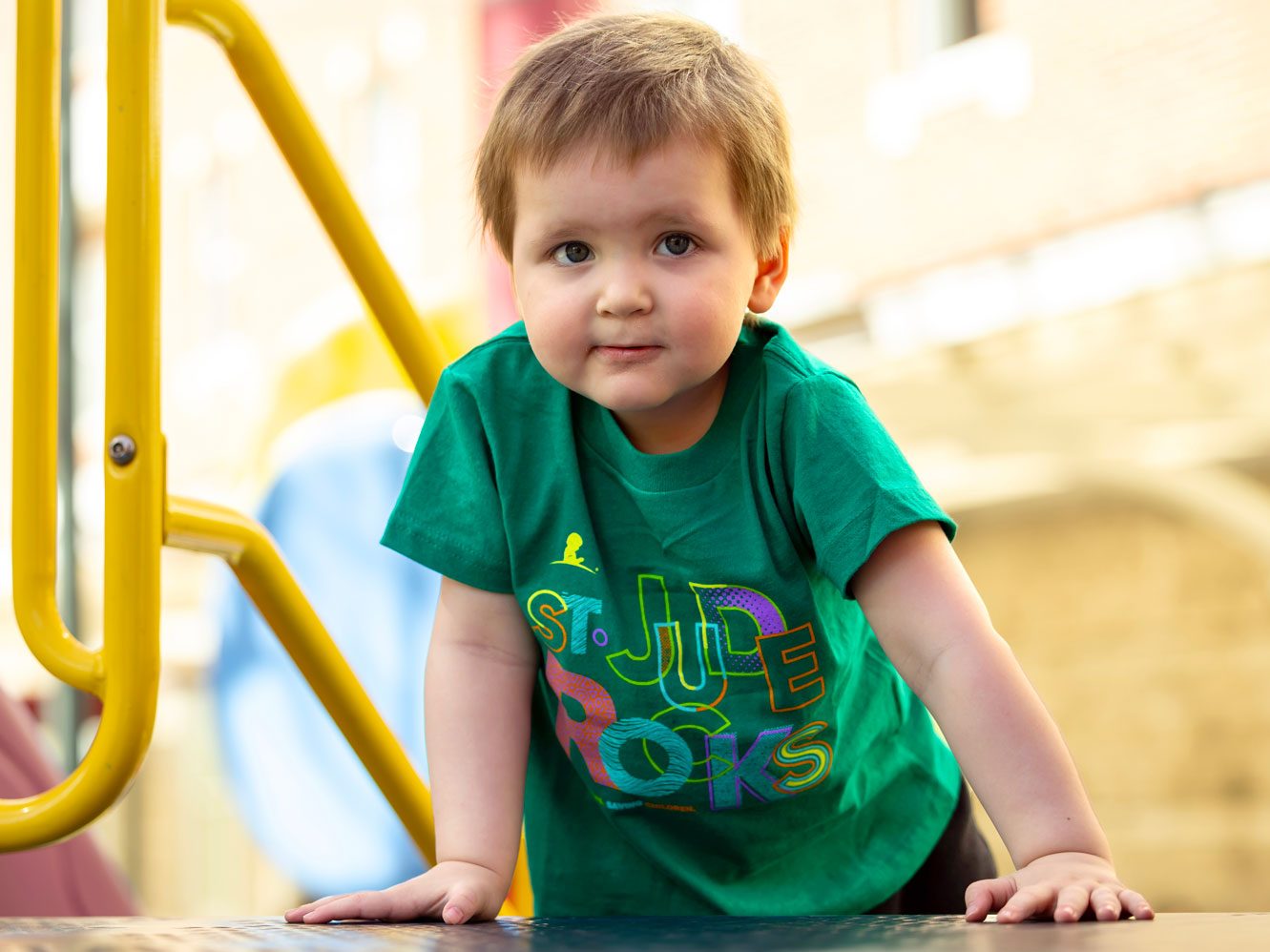 James St. Jude patient James wears a green St. Jude T-shirt and climbs on colorful playground equipment.