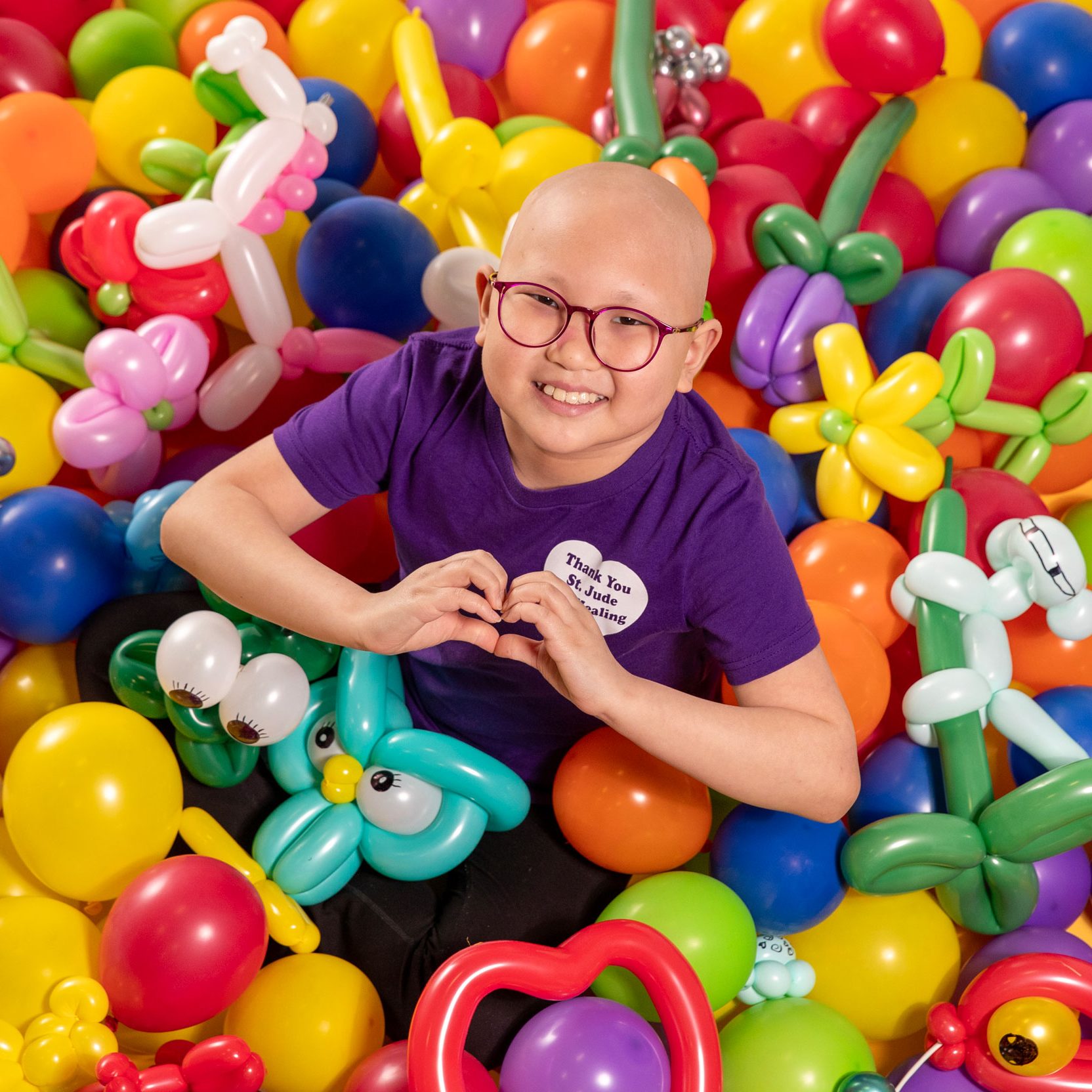 St. Jude patient Misheel makes a heart sign with her hands in this overhead photo taken with her balloon art creations.