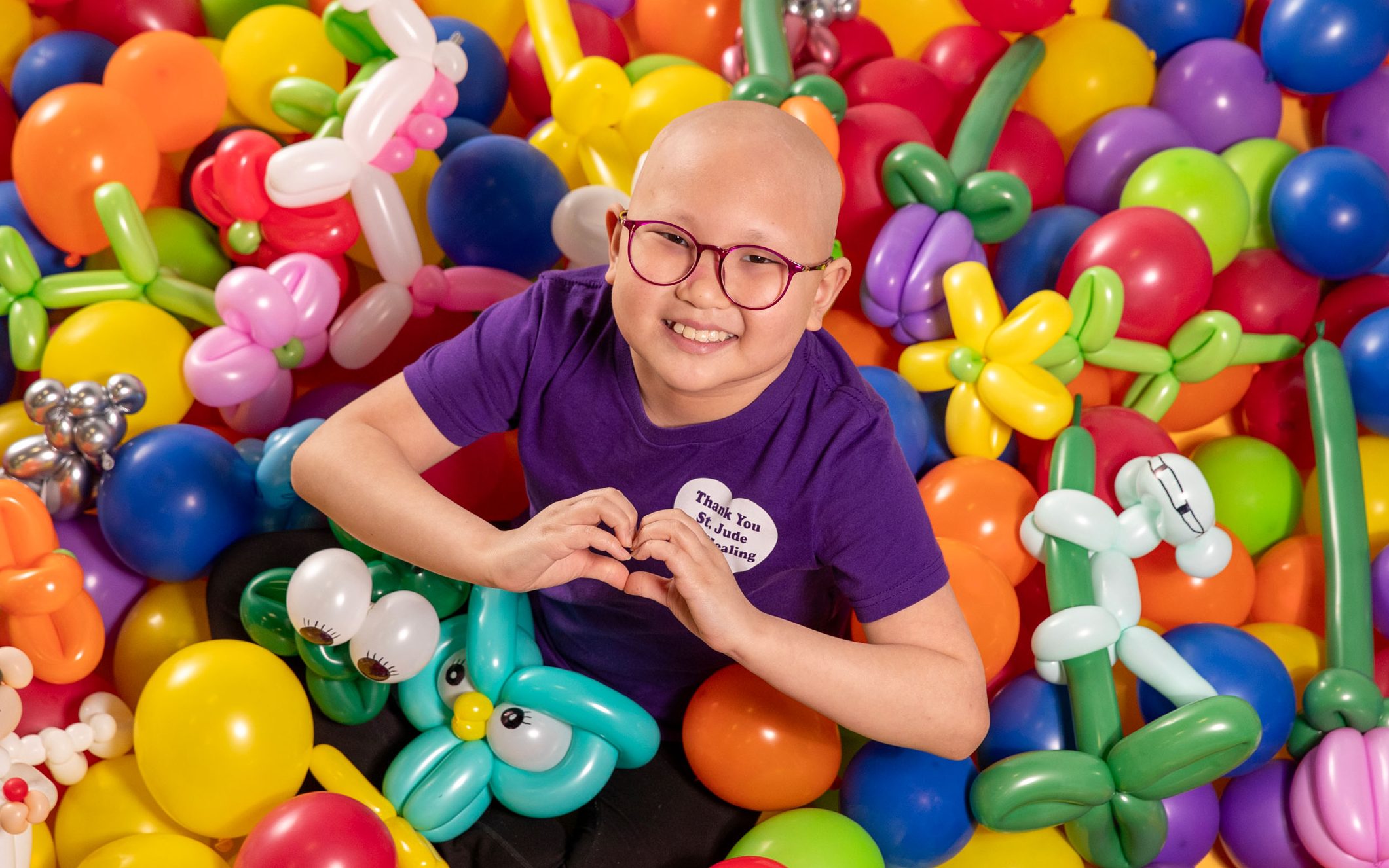 St. Jude patient Misheel makes a heart sign with her hands in this overhead photo taken with her balloon art creations.