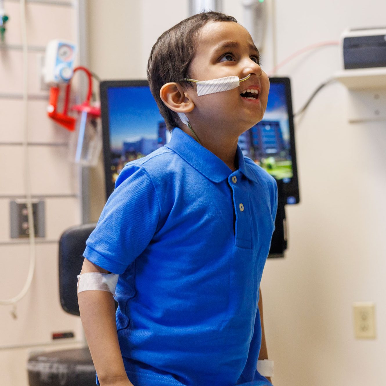 St. Jude patient Aditya shown in a treatment room wearing a royal blue polo shirt.