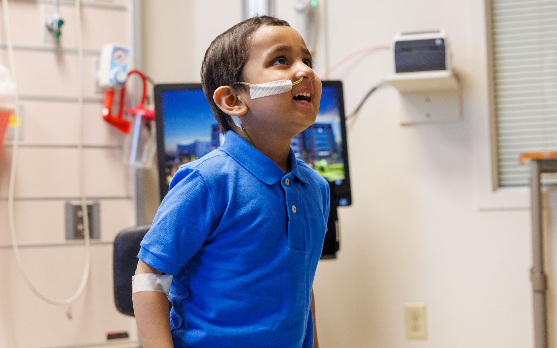 St. Jude patient Aditya shown in a treatment room wearing a royal blue polo shirt.