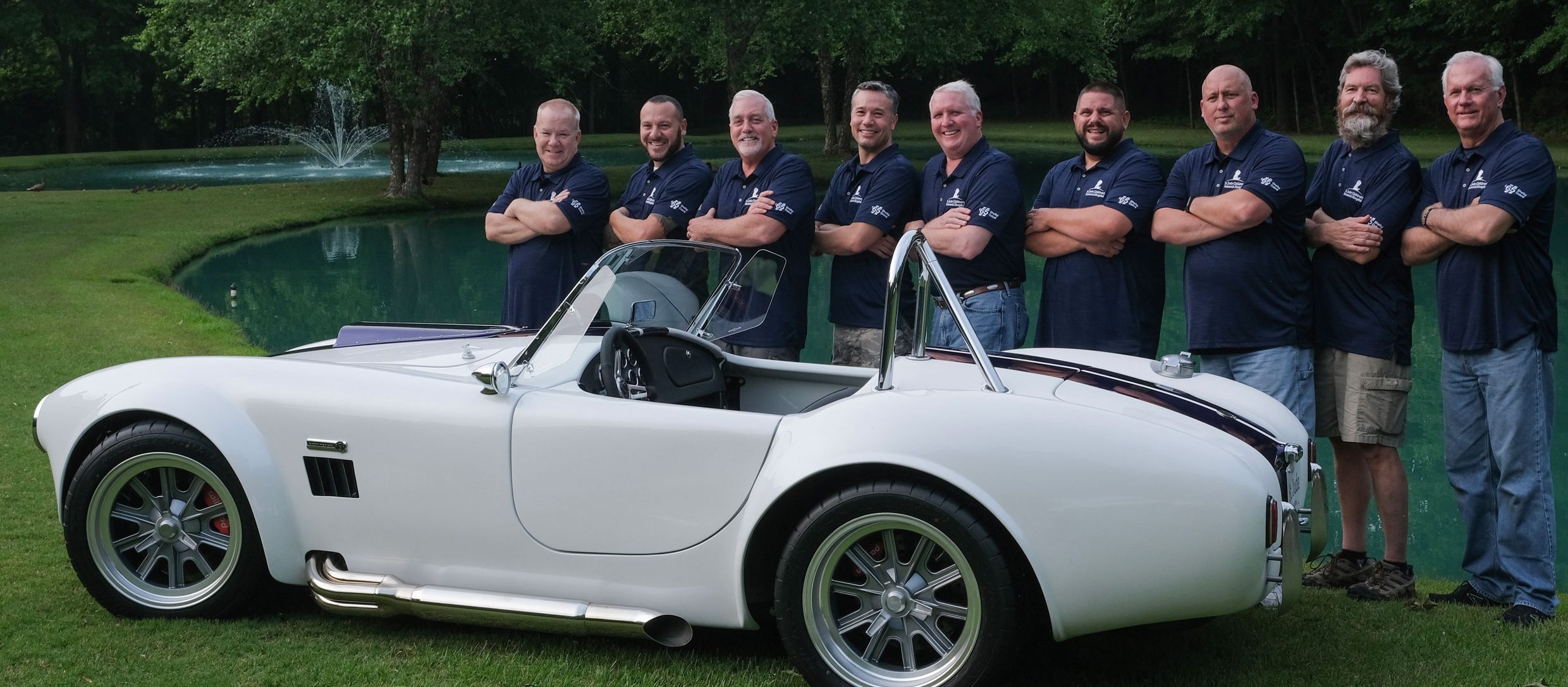 A brightly-painted car sits on a golf course with several of its builders standing nearby