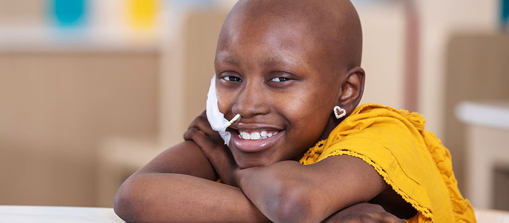 Patient Kenadie rests her head on her crossed arms as she smiles in a colorful room.