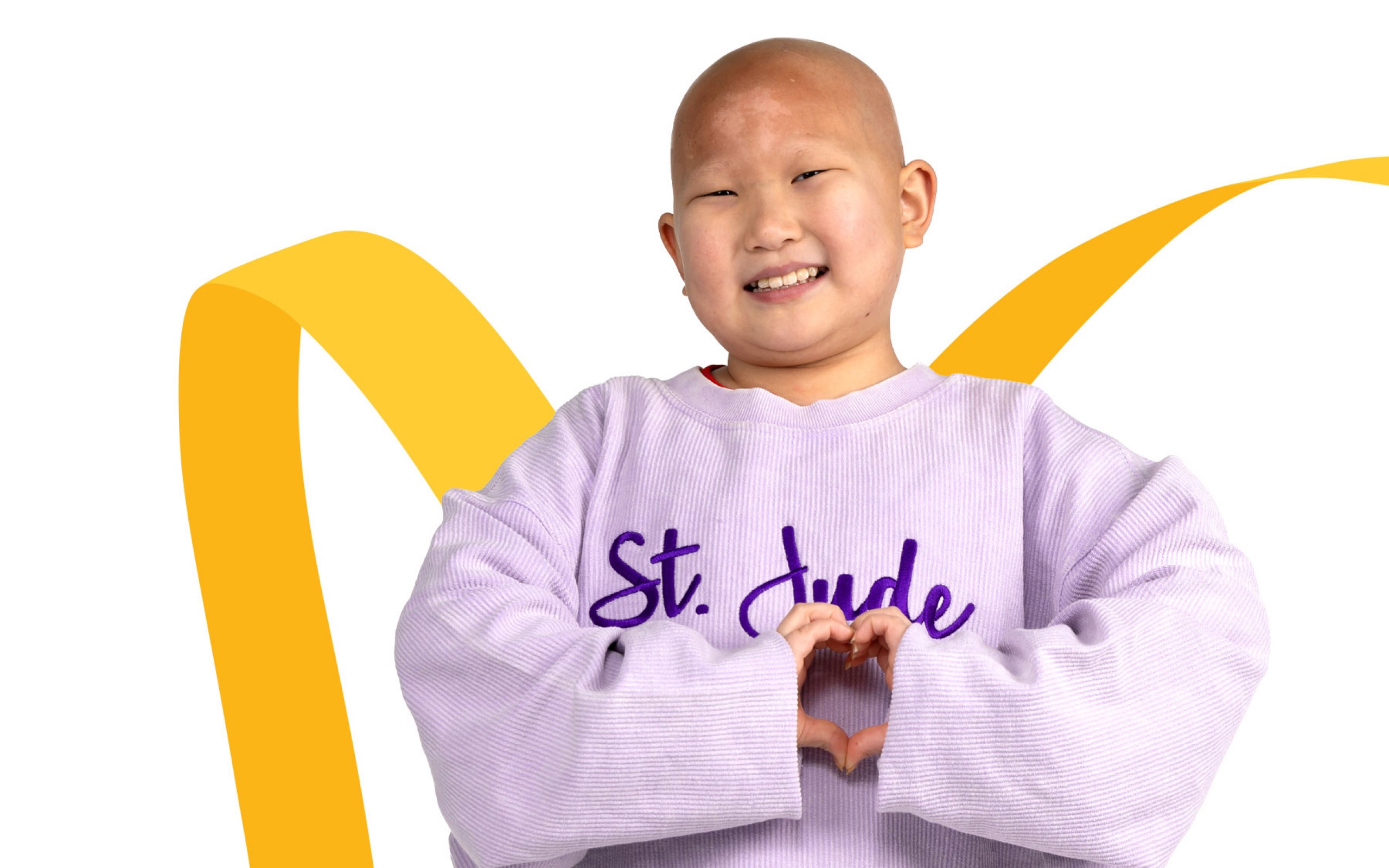 St. Jude patient Misheel making a heart with her hands in front of a gold ribbon.