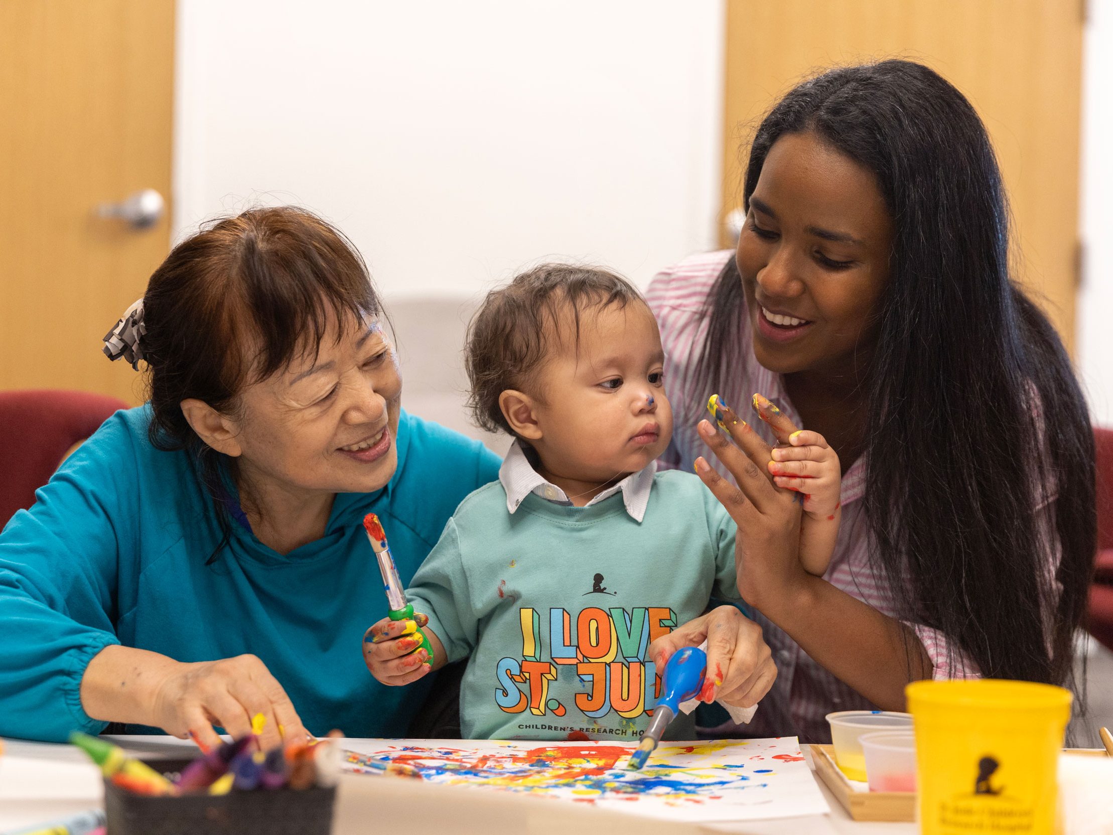 St. Jude patient Han paints a picture with the help of his mother and grandmother.