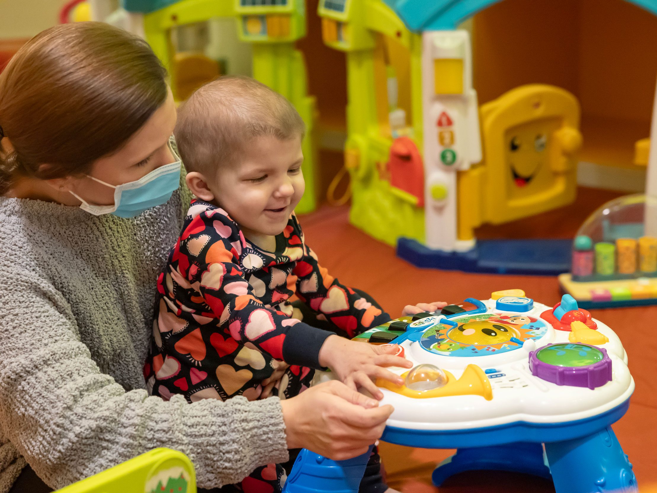 St. Jude patient Logan sits in her mother's lap and plays with a toy.
