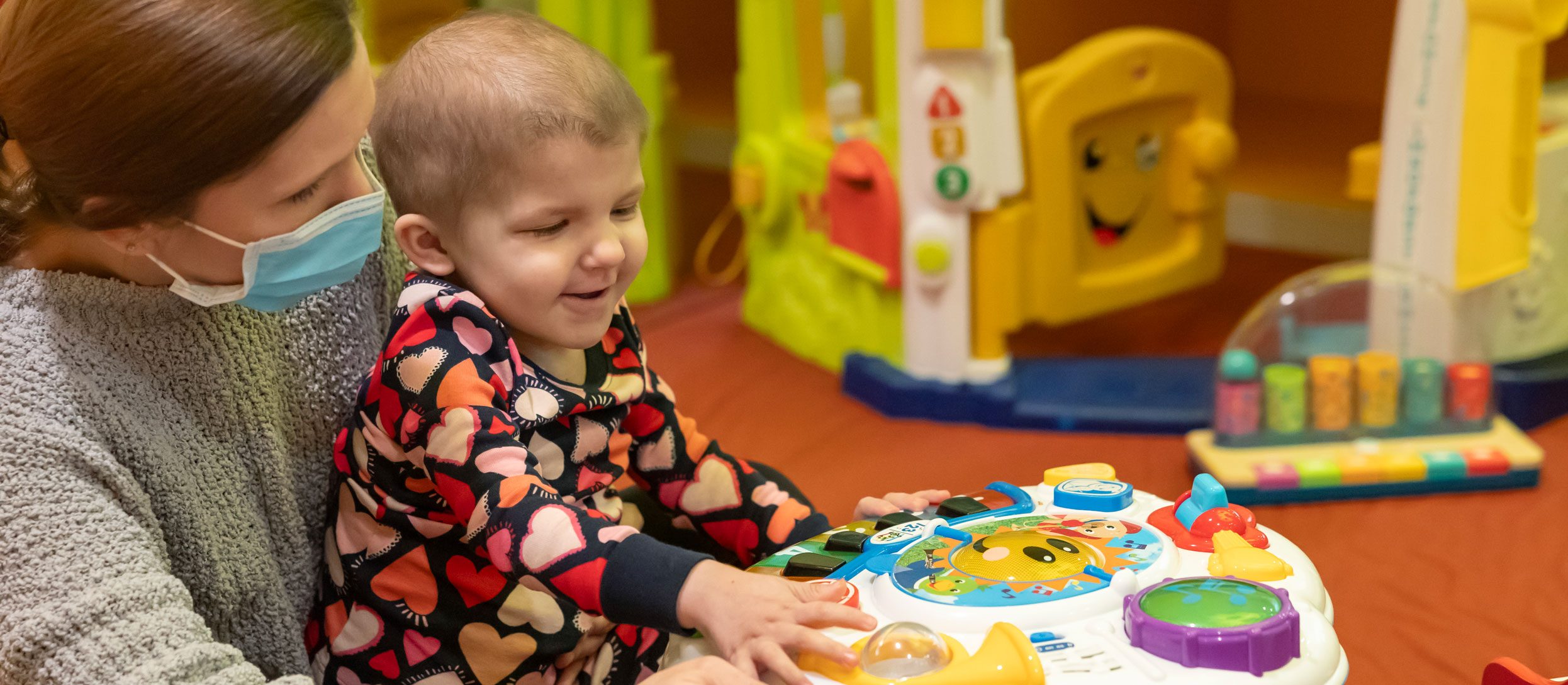 St. Jude patient Logan sits in her mother's lap and plays with a toy.