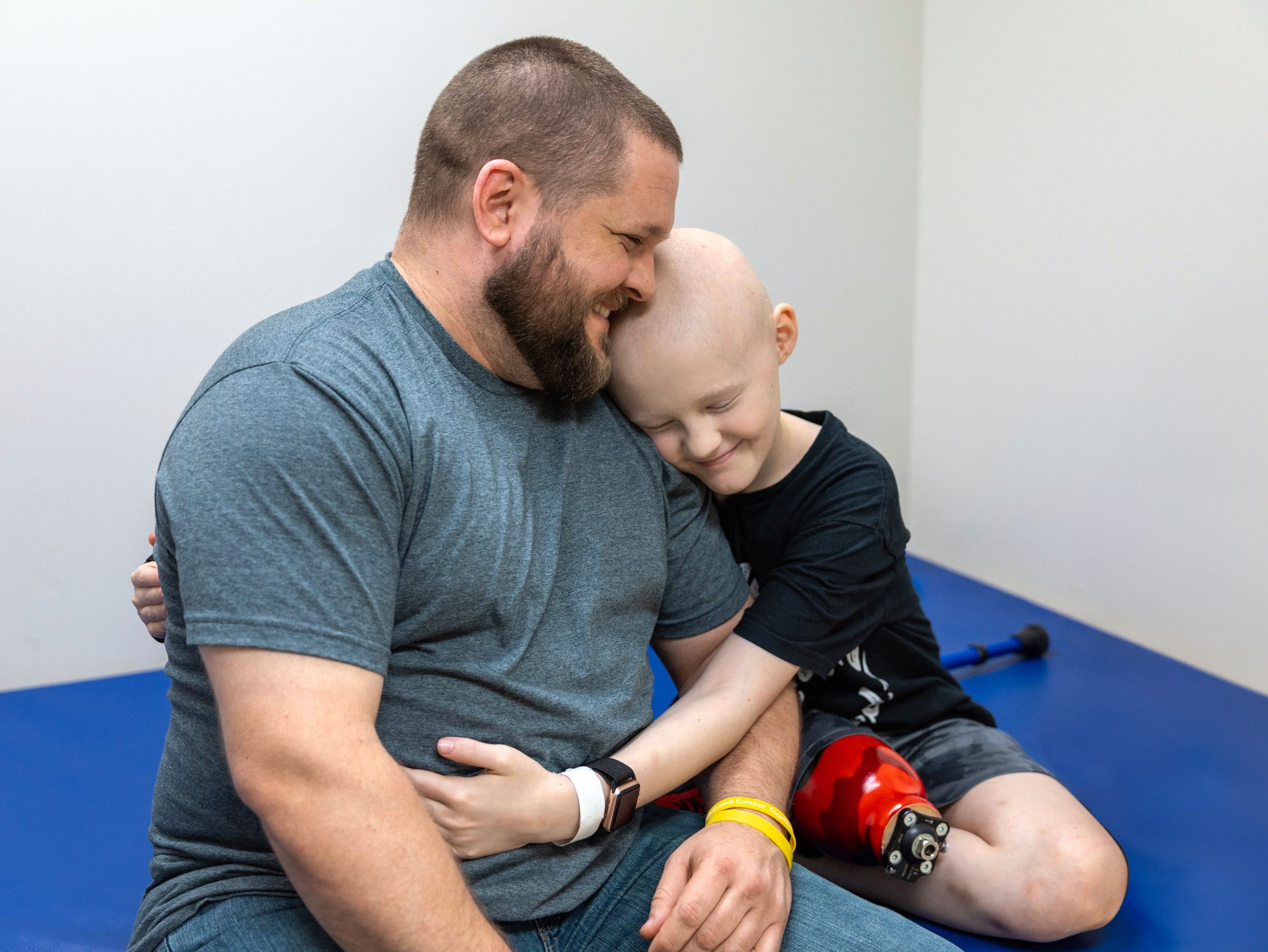 St. Jude patient Hunter sitting on an exam table hugging his father.