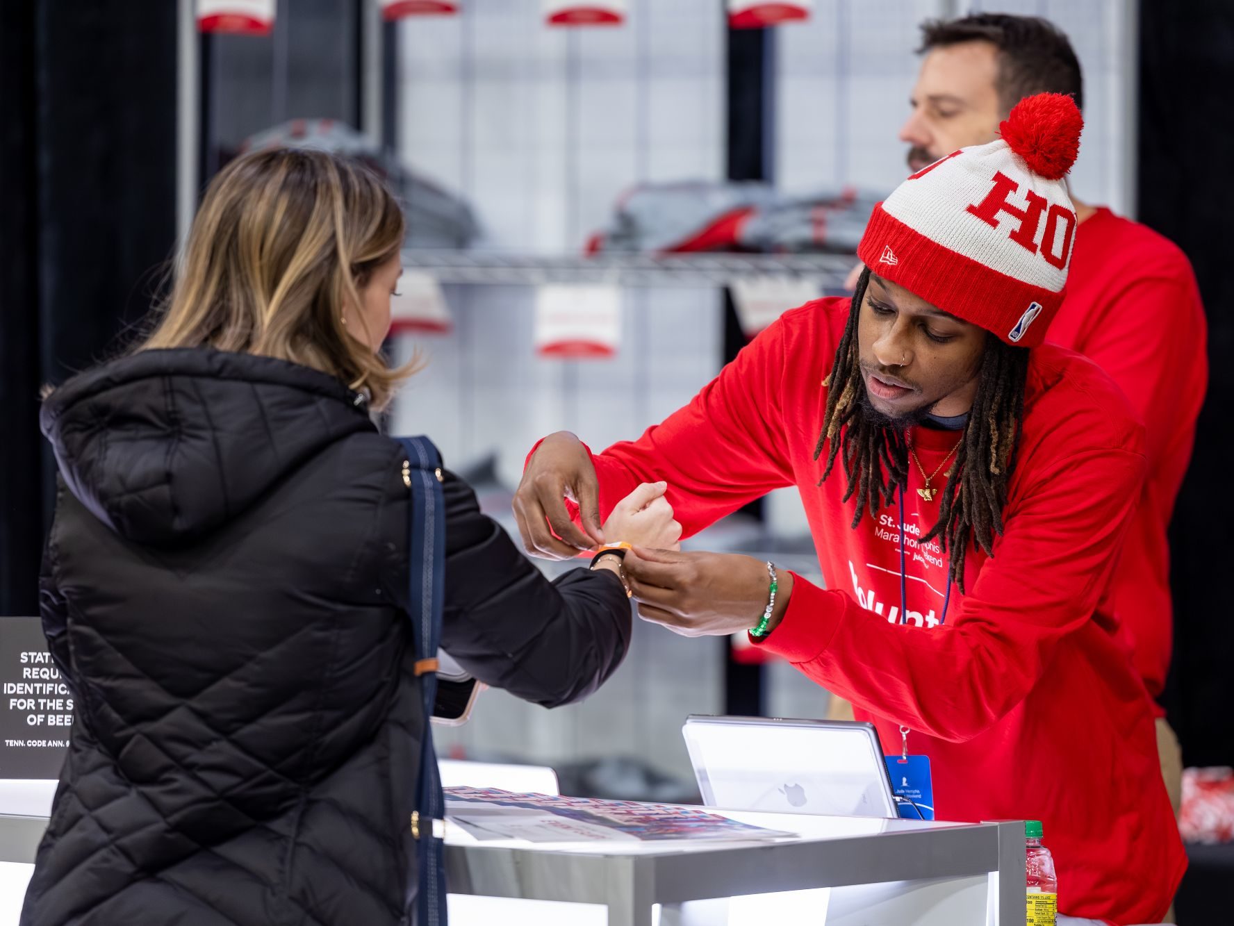 A St. Jude volunteer in a red volunteer shirt helps a participant with an wristband at the St. Jude Memphis Marathon Expo.