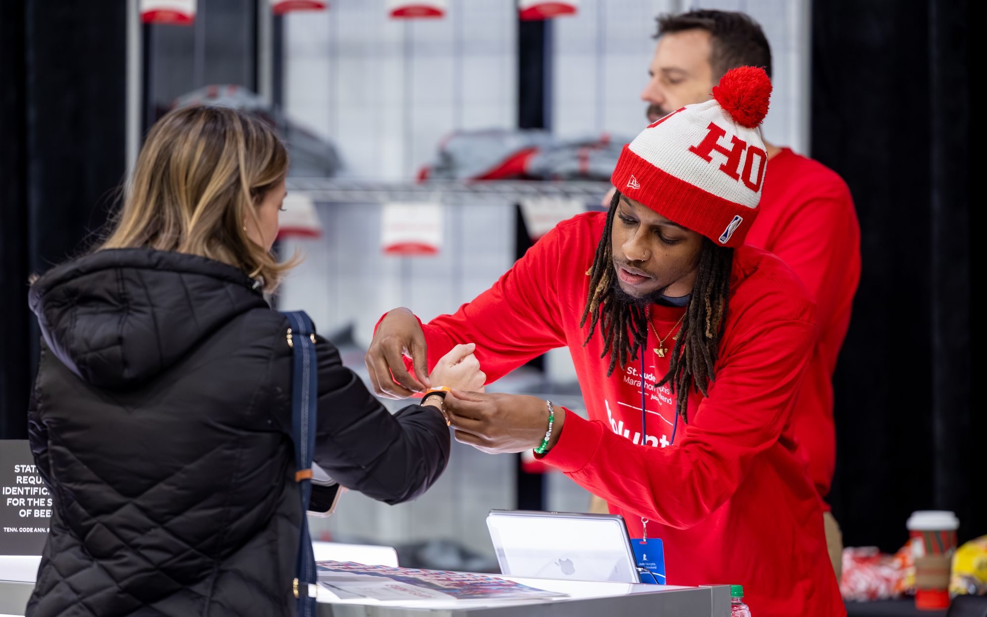 A St. Jude volunteer in a red volunteer shirt helps a participant with an wristband at the St. Jude Memphis Marathon Expo.