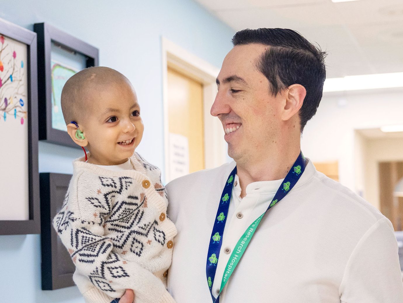 St. Jude patient Emmanuel is held by his father in a hallway with colorful art on the walls.