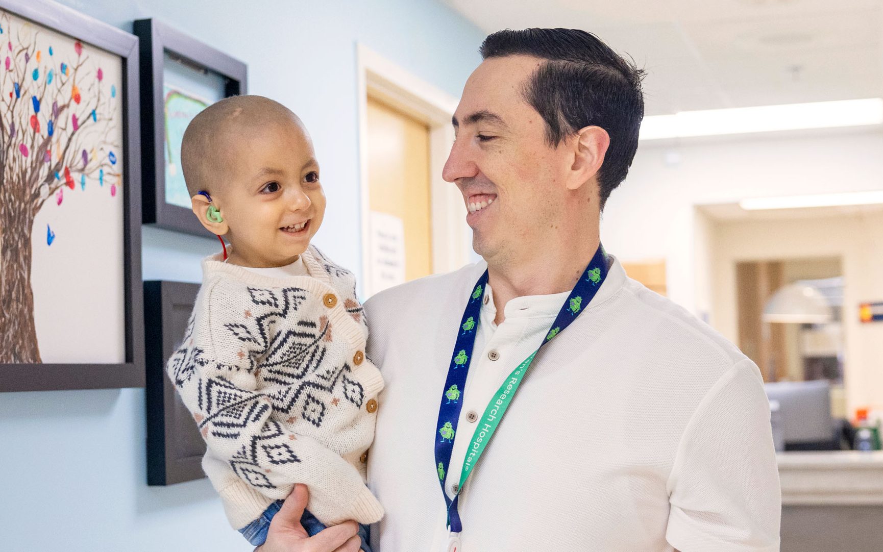 St. Jude patient Emmanuel is held by his father in a hallway with colorful art on the walls.