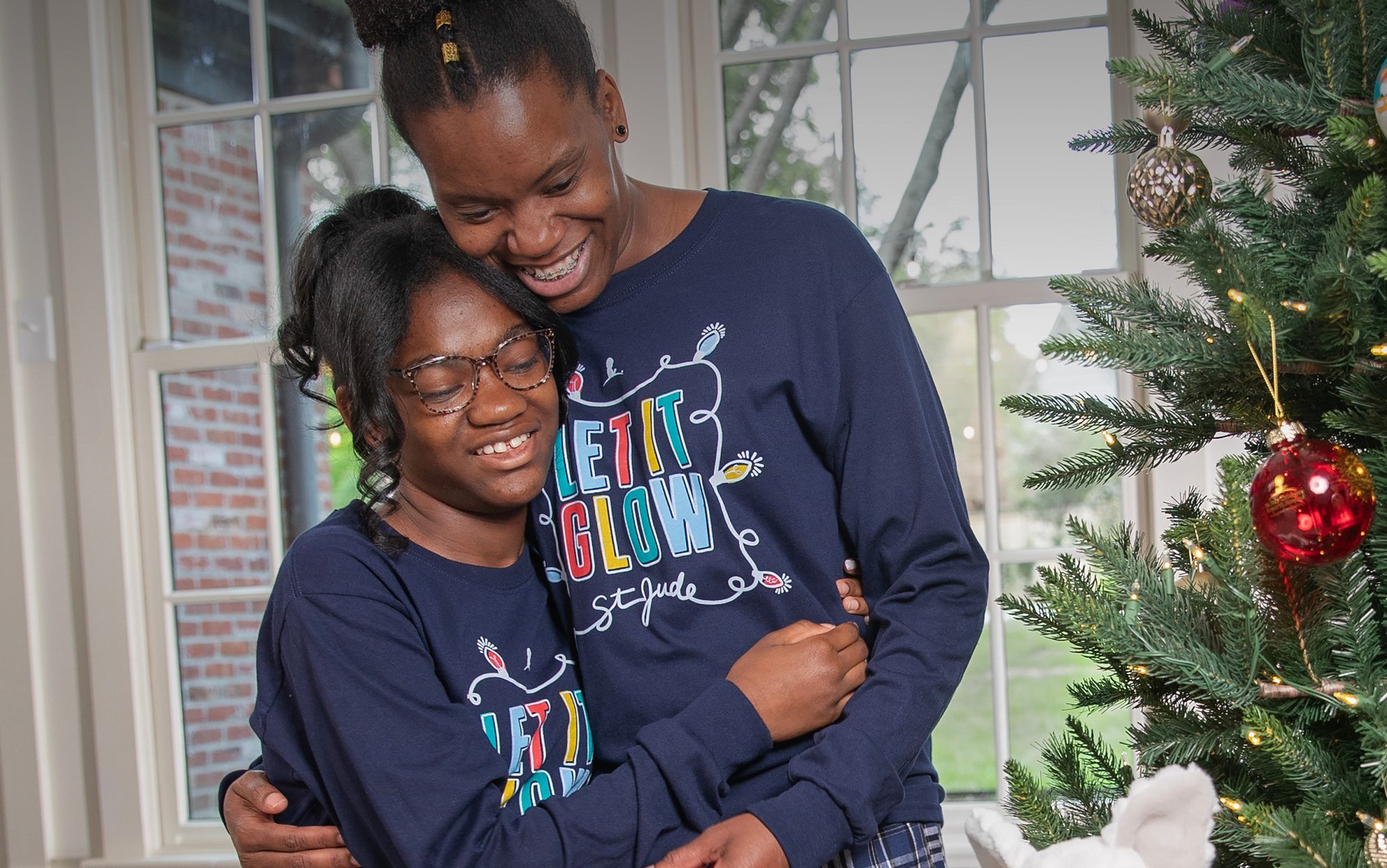 St. Jude patient Alana and her mom by a Christmas tree with presents.