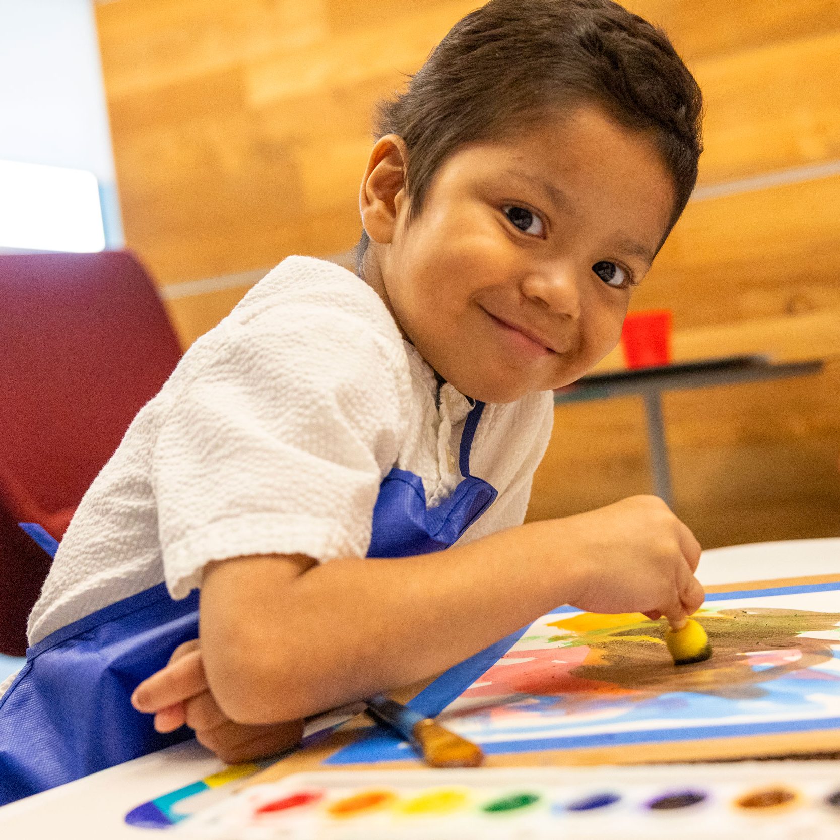 Juan, paciente de St. Jude de Guatemala, sonriente mientras pinta un cuadro con muchos colores.