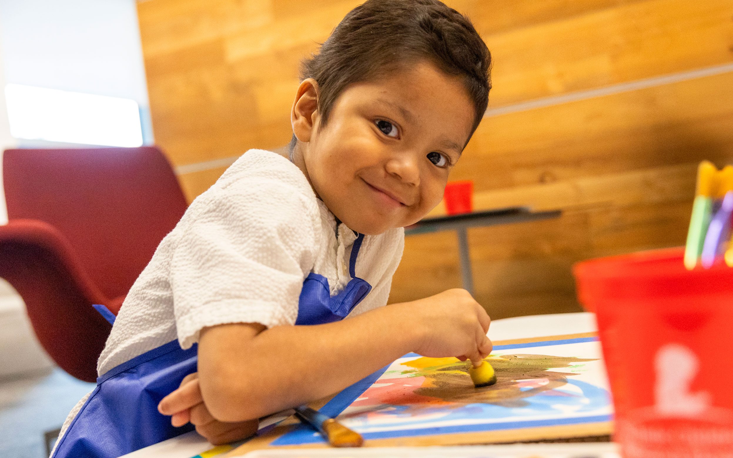 Juan, paciente de St. Jude de Guatemala, sonriente mientras pinta un cuadro con muchos colores.