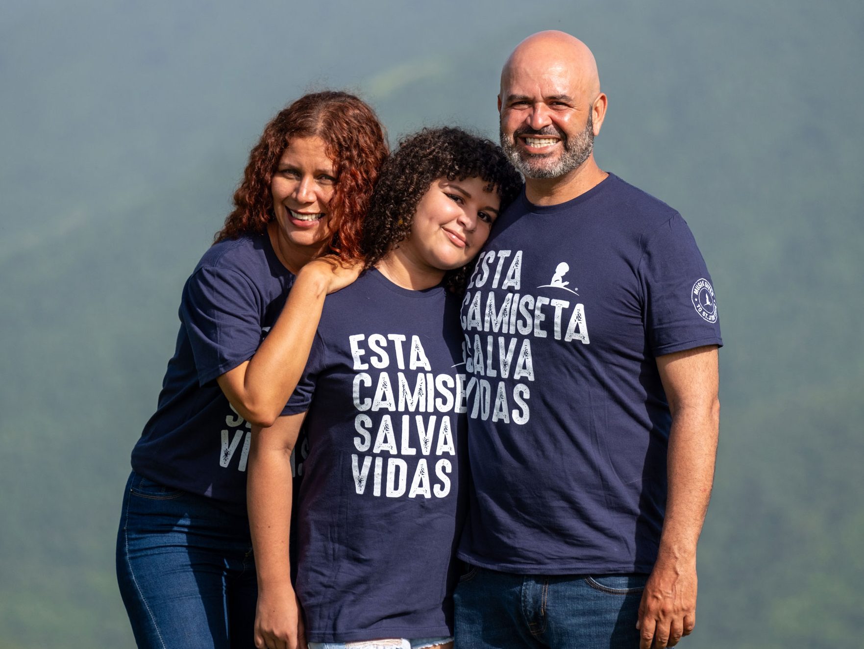 Yamila, paciente de St. Jude, aparece de pie entre sus padres, con un hermoso paisaje natural como fondo.
