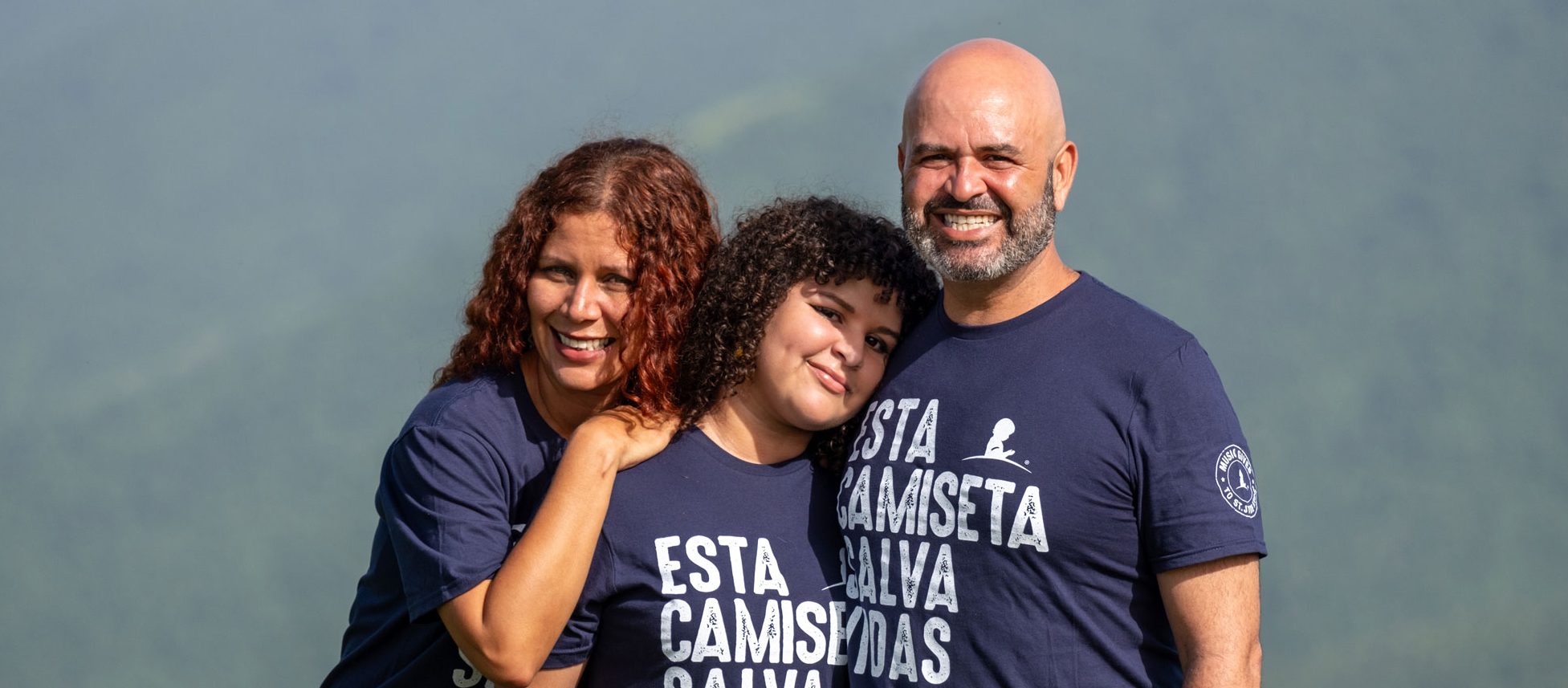 Yamila, paciente de St. Jude, aparece de pie entre sus padres, con un hermoso paisaje natural como fondo.