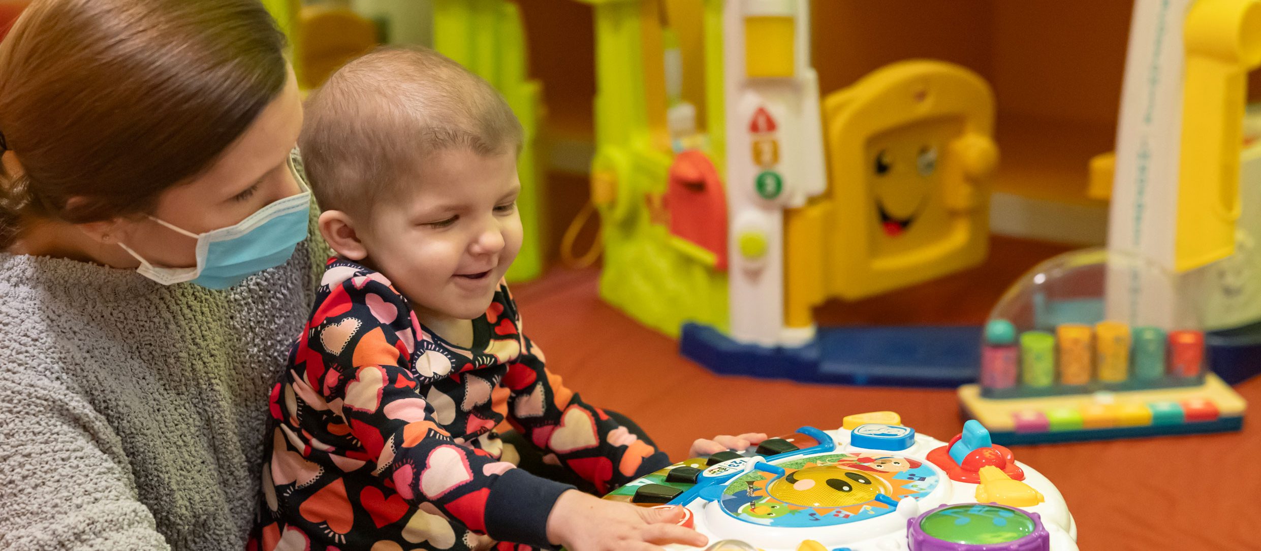 Logan, paciente de St. Jude,  con su mamá, disfruta en un salón de juegos rodeado de una gran variedad de juguetes.