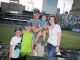 A family poses in front of the baseball field.