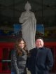 A woman and a man standing in front of the St. Jude Thaddeus statue