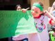 A sibling star from the green team holding up a sign that says "Go Green! We are the team!"