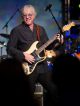 Mike Mills smiles and plays guitar.