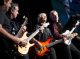 Four men with guitars jam together on stage.