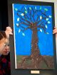 A girl presents a painting of a popsicle stick tree with construction paper leaves with inspirational words written on them