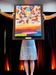 Girl holding up a brightly colored painting with geometric shapes, paint splatters, and wide brush strokes
