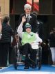 A young man being wheeled down the blue carpet in his tuxedo.