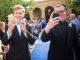 Two young men in tuxedos take photos as they walk the blue carpet.