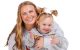 St. Jude patient Mila, wearing her hair in pigtails, is embraced by her mother and smiles.