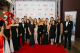 St.Jude Celebrity Chef and Wine Dinner attendees pose before  a wall emblazoned with sponsor logos. 