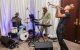 A band performs on drums, keyboards, and trumpet. 