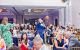 A live auctioneer points across a ballroom, and event attendees raise ballot numbers in the air. 