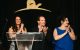 Three presenters smile and applaud onstage at St. Jude Evening with the Stars charity gala. 