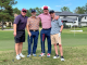 Four men standing in front of a building with their golf clubs smiling