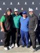 Four men standing in front of a building with their golf clubs smiling