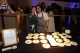 Wall Street Taste of New York caterers smile behind a table covered with slices of cake. 