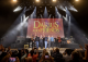 Darius Rucker and other musicians stand on stage and raise their arms during Darius and Friends. 