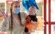 St. Jude patient Mila wears a colorful outfit and is held by her mother, who is wearing a surgical mask.