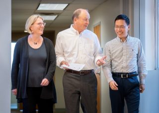 St. Jude researchers Nichols, Robison and Wang walk down a hallway discussing the latest scientific advances.