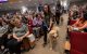 Women walk two service dogs down an aisle at a crowded auditorium as onlookers smile