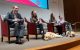 Two service dogs sleep at the feet of four adults who are sitting in chairs in an auditorium