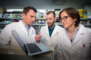 St. Jude researchers Northcott, Smith and Bihannic in white lab coats huddle around laptop