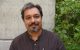 Aseem Ansari, PhD, standing in front of a concrete wall with greenery behind him
