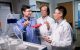 Three scientists in lab coats discuss samples in test tubes for their latest work