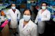 The researchers wearing masks and lab coats stand in a lab together.